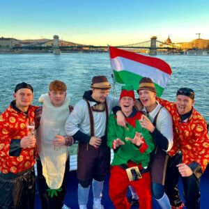 Five people toasting with beer glasses on a boat at sunset, enjoying a festive atmosphere during a stag boat cruise, during a budapest stag do.