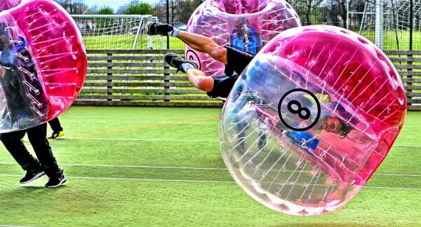 Players in inflatable bubbles bouncing and tumbling on a football field, showcasing the fun and chaos of bubble football Budapest stag activities