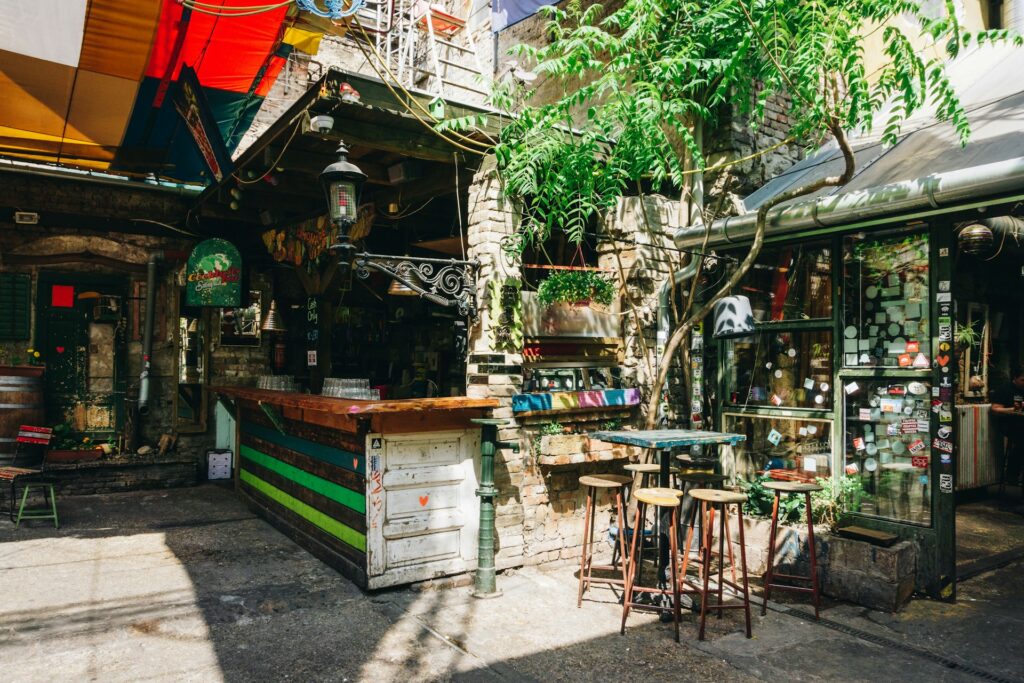 This image showcases a vibrant and eclectic outdoor bar or café in Budapest, perfect for stag do activities, with colorful decor, rustic furniture, and a lively atmosphere.
