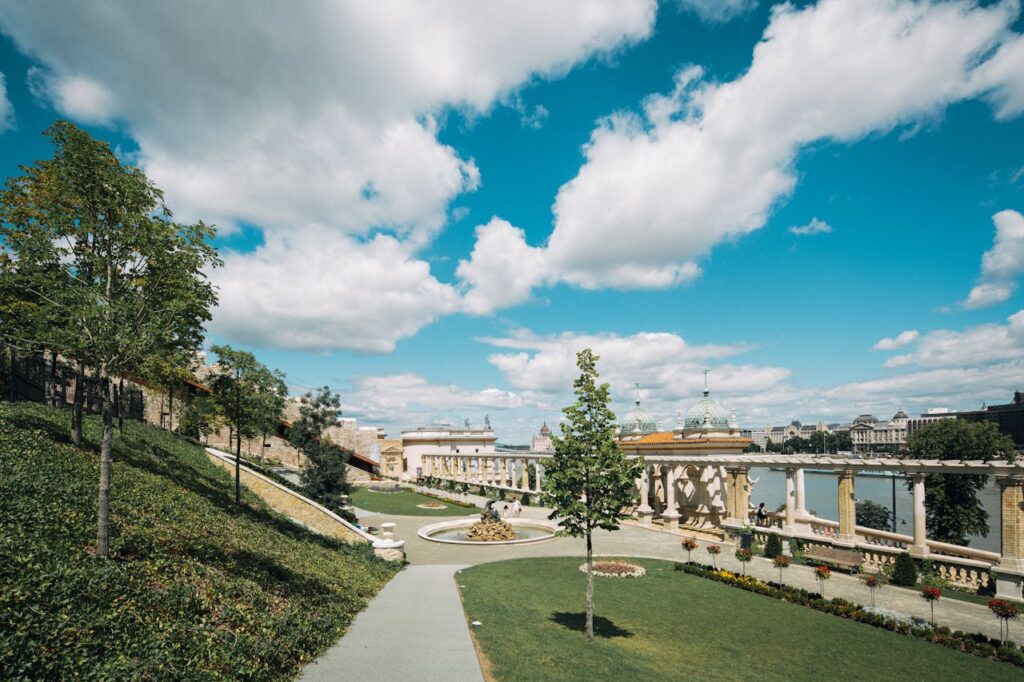 A beautiful park with lush greenery, historic architecture, and a clear blue sky in Budapest.