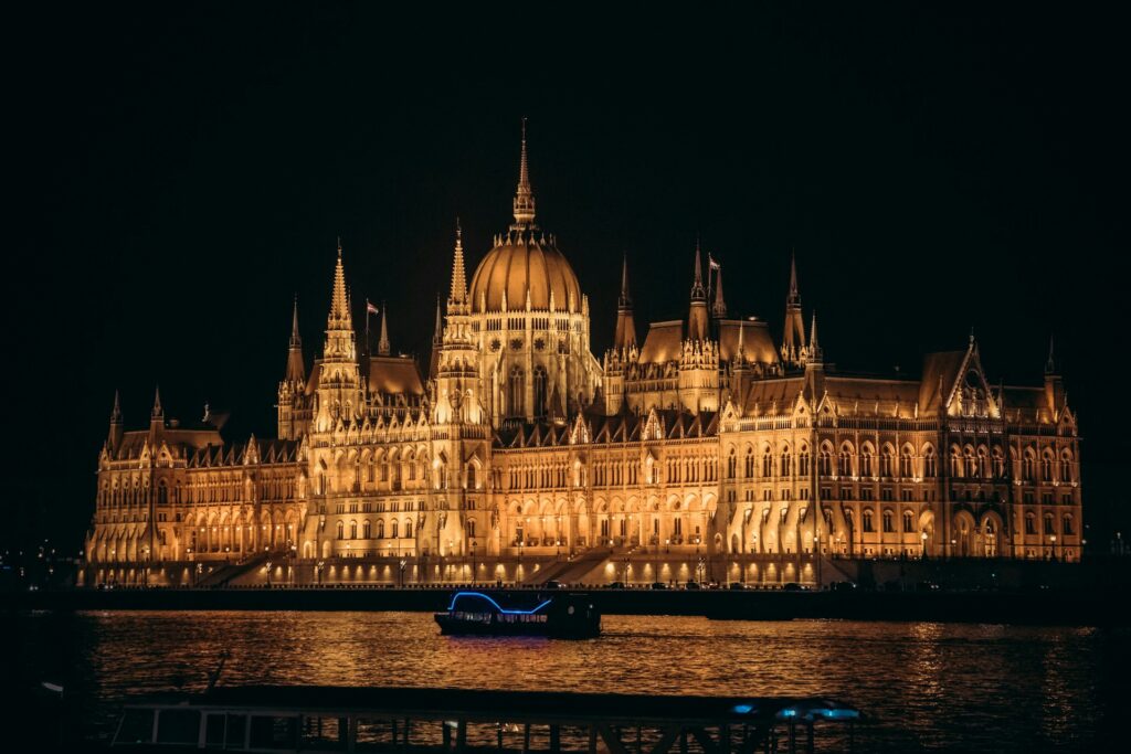 This is a breathtaking night view of the Hungarian Parliament Building in Budapest, beautifully lit, with a boat on the Danube, ideal for a lively boat party experience.